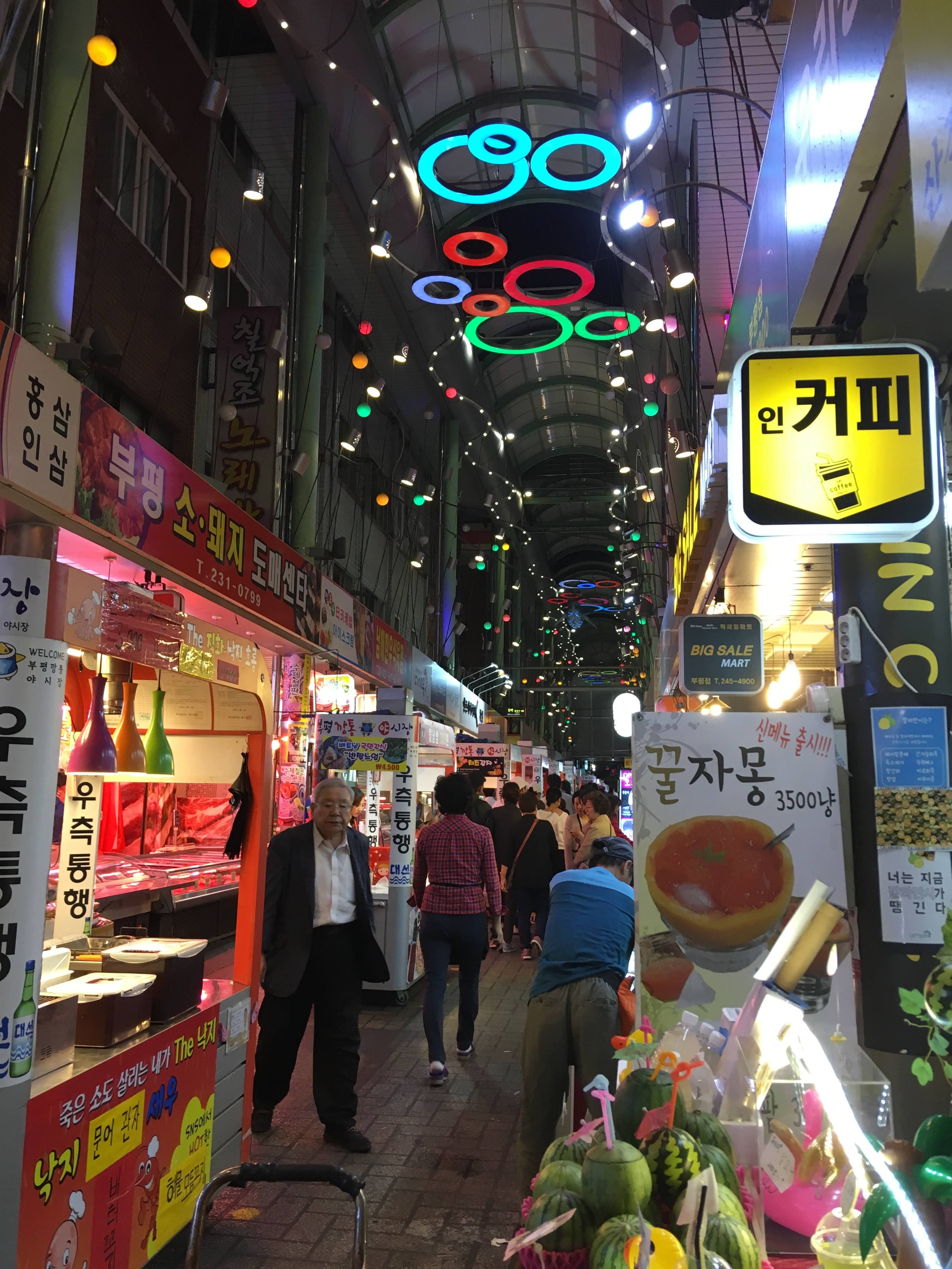 Covered arcade of Bupyeong Kkangtong Night Market lit by neon signage and crowded with shoppers