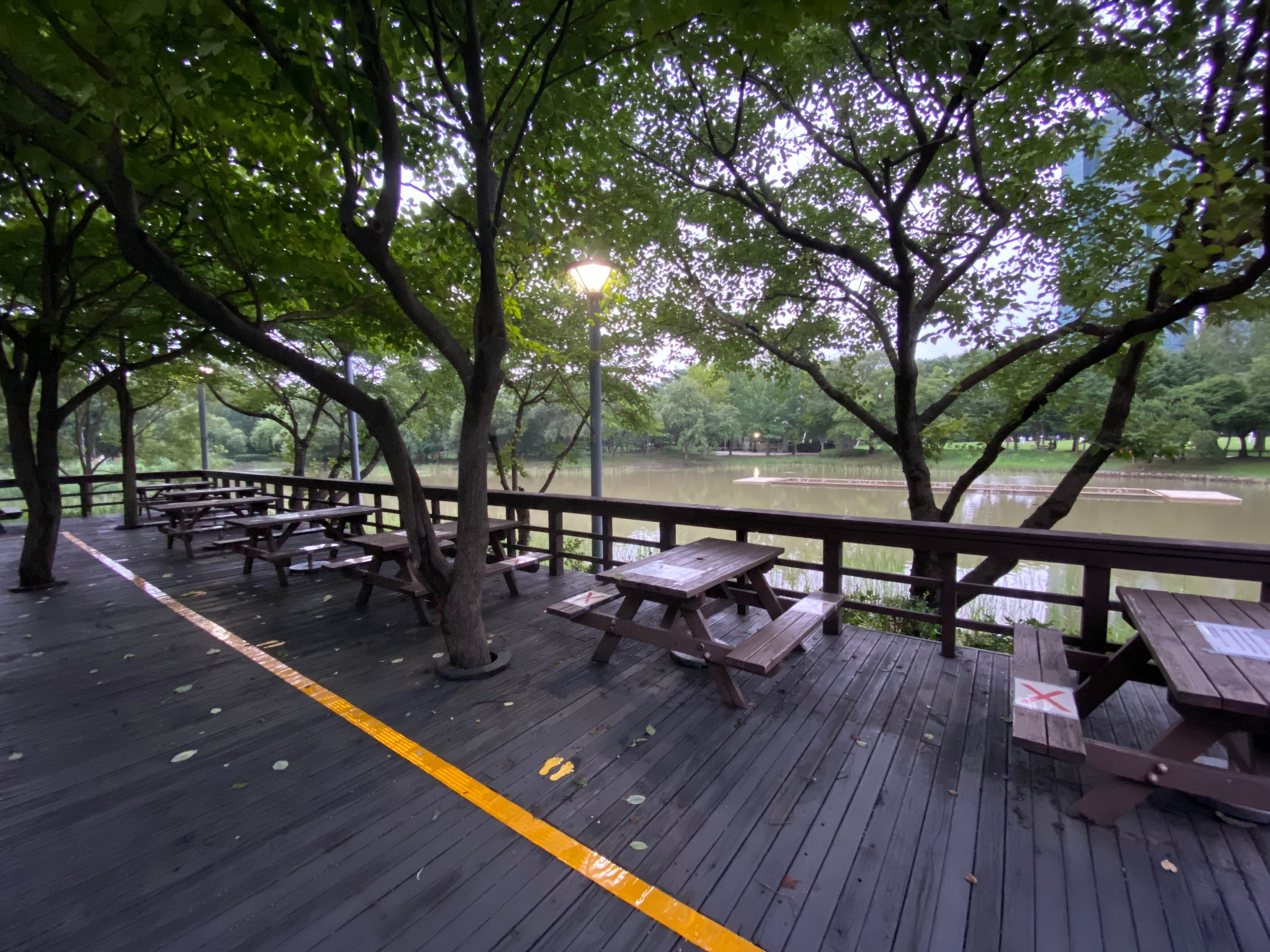 Picnic tables on a shaded boardwalk deck beside a pond in Seoul Forest