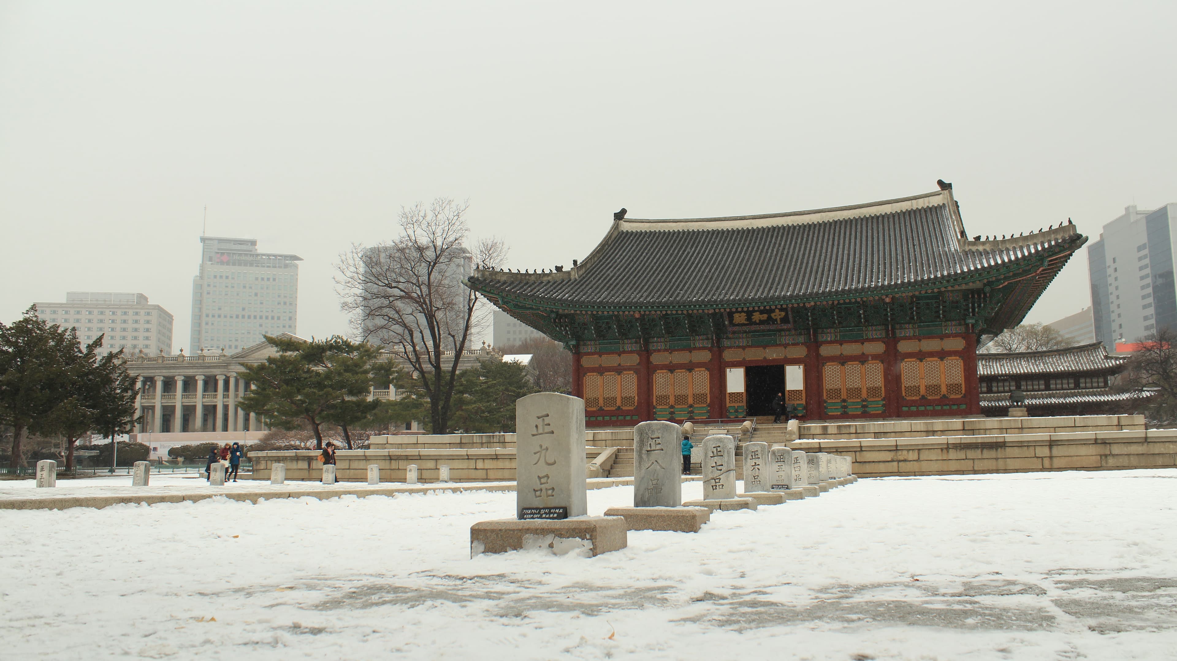 Junghwajeon at Deoksugung Palace under snow, with the modern city skyline behind it