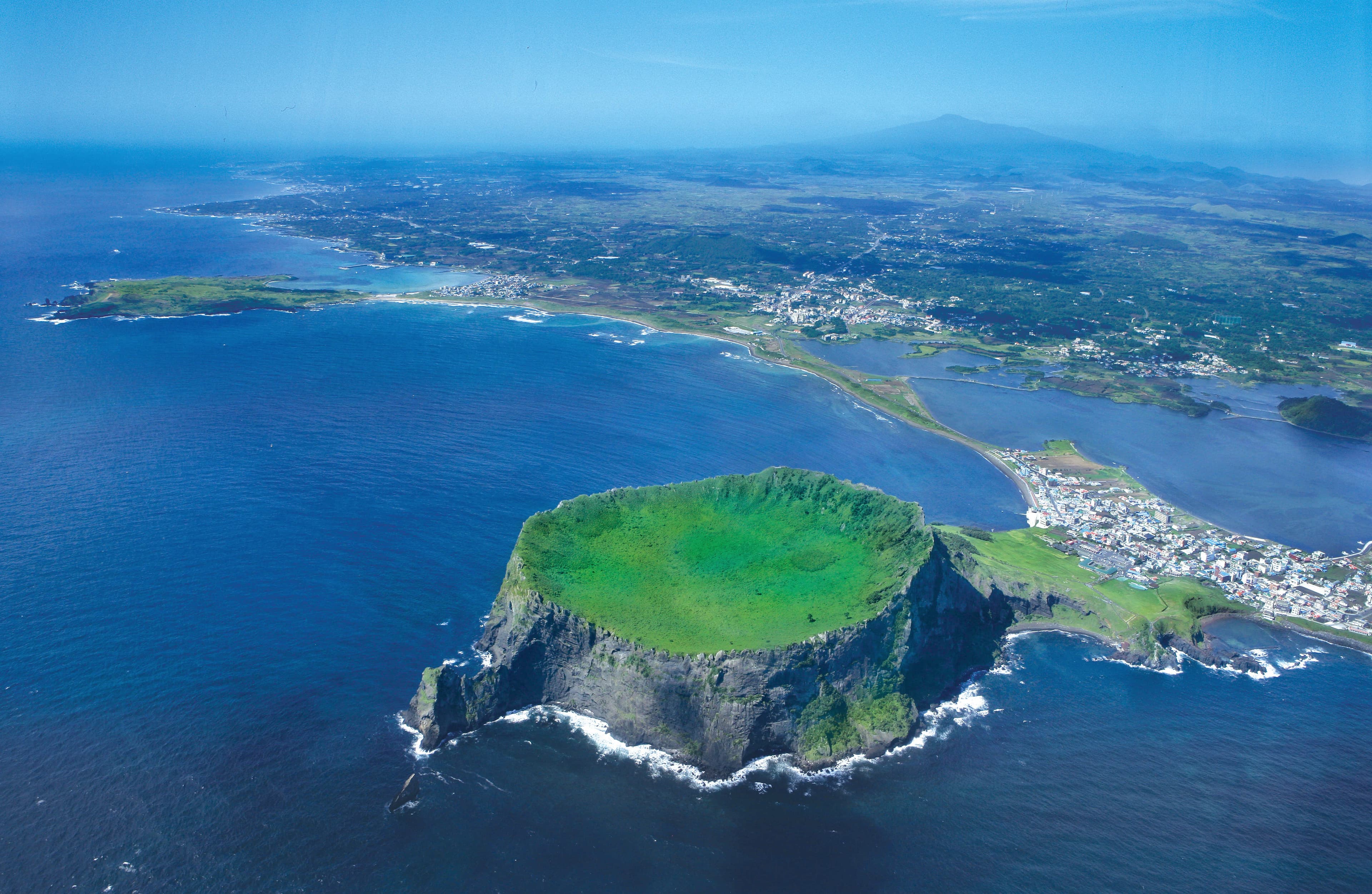 Aerial view of Seongsan Ilchulbong's crater, with Hallasan visible in the distance