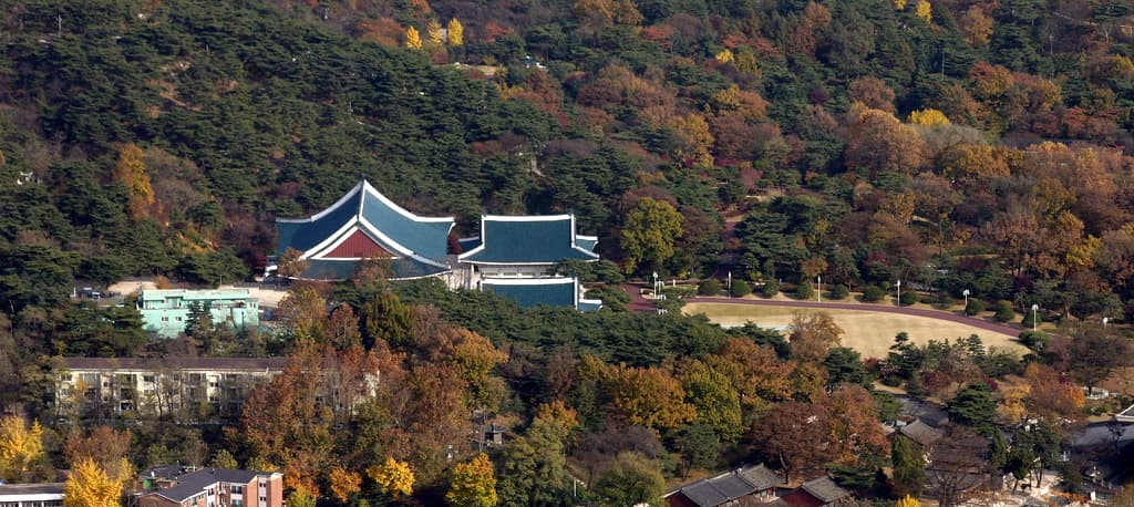 The Blue House's main hall set among autumn foliage, with Mount Bukhan behind it
