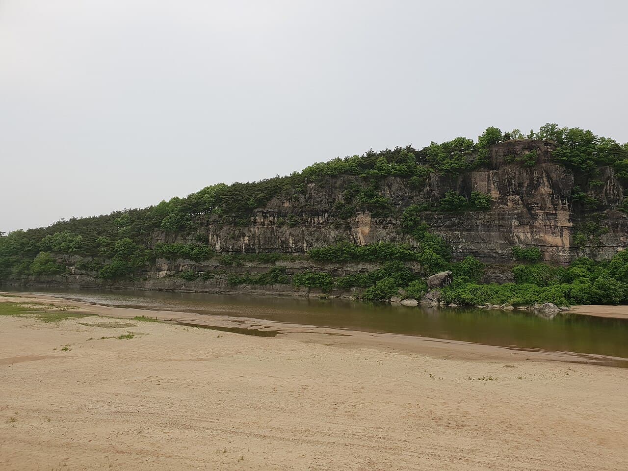 The layered rock face of the Buyongdae cliff above the Nakdong River, seen across the white sandbank on the Hahoe side
