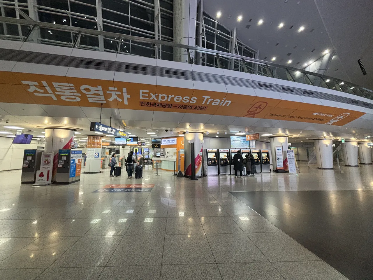 The airport railway concourse in Incheon Airport Terminal 1's transportation centre, with ticket machines and a service desk under an orange Express Train banner